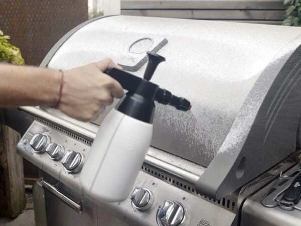 Spezialisierter Grillreiniger wird mit einer Pumpsprühflasche auf die Grillhaube aufgetragen