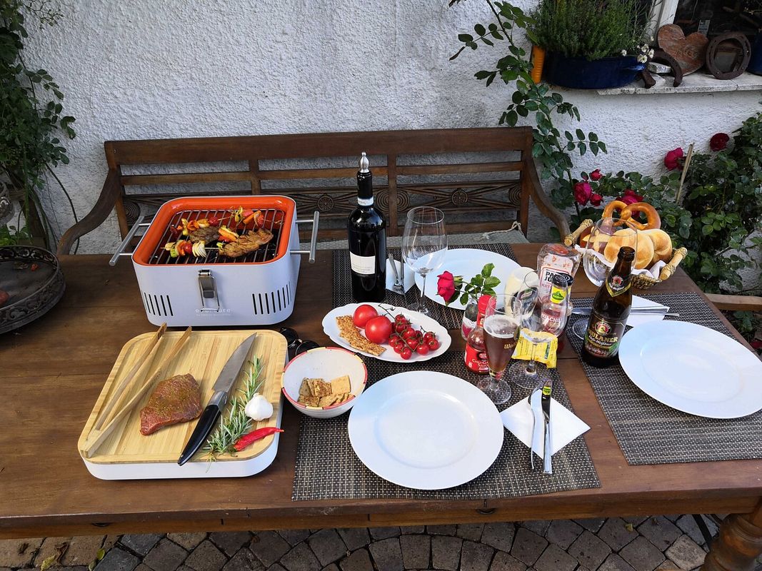 Voller Grillrost, Gedeckter Tisch, Schneidebrett mit Grillzange, Messer, Stück Rinderfilet, Rosmarin, Knoblauch und Chili